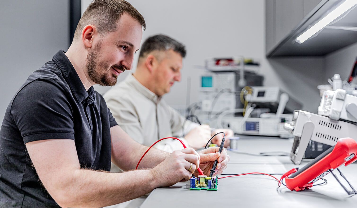 Deux techniciens dans un laboratoire d'électronique, effectuant des tâches d'assemblage de précision dans des conditions d'éclairage adaptées