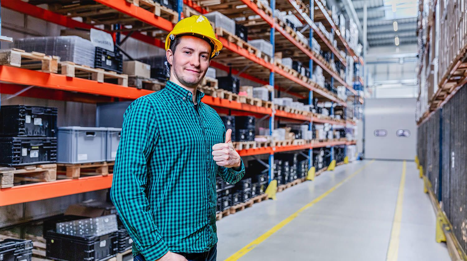 Un employé de l'entrepôt, souriant et levant le pouce, souligne l'importance d'un bon éclairage pour le confort et l'efficacité au travail.