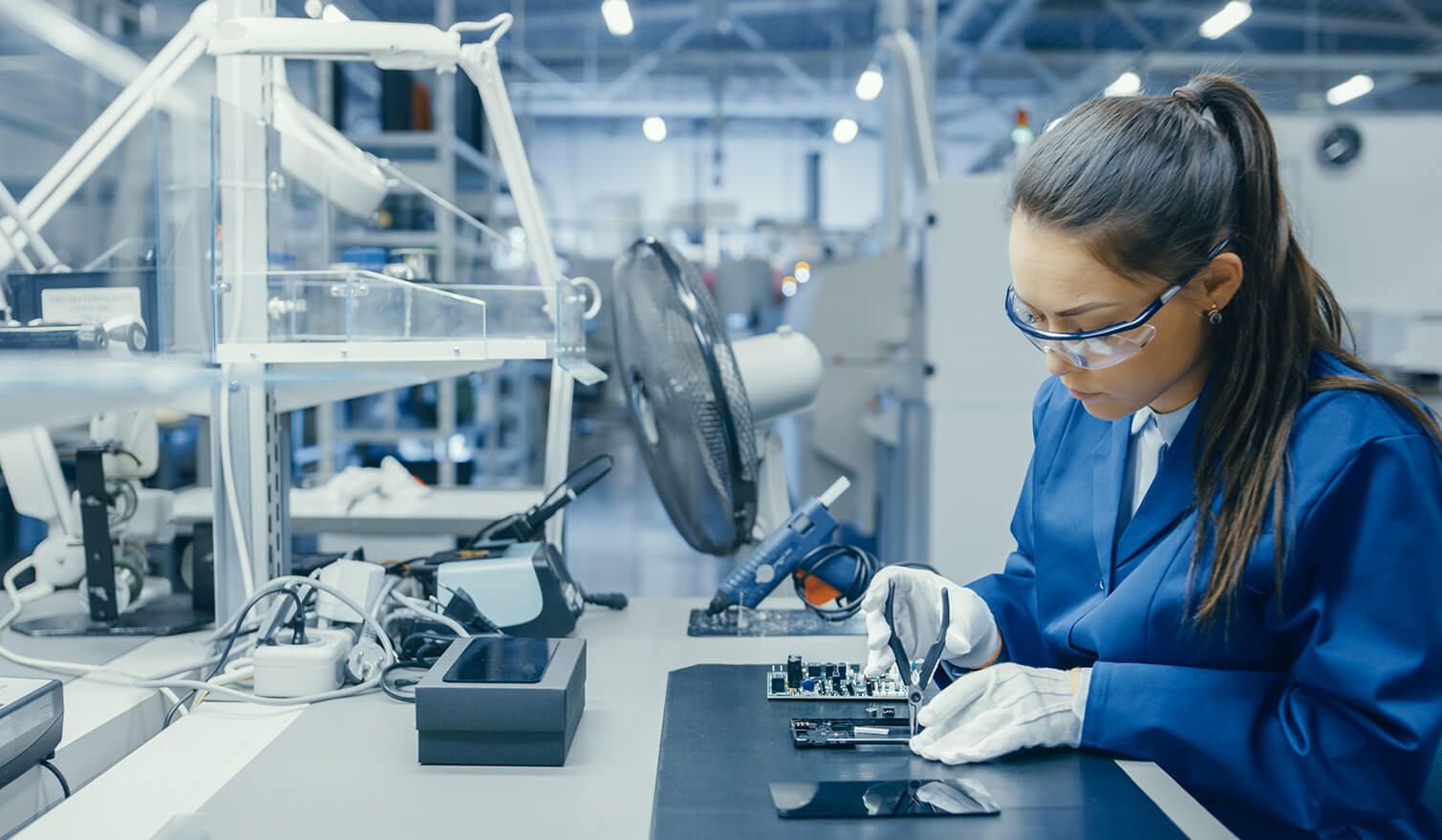Une femme en tenue bleue manipule avec précision du matériel électronique dans un environnement de production correctement éclairé