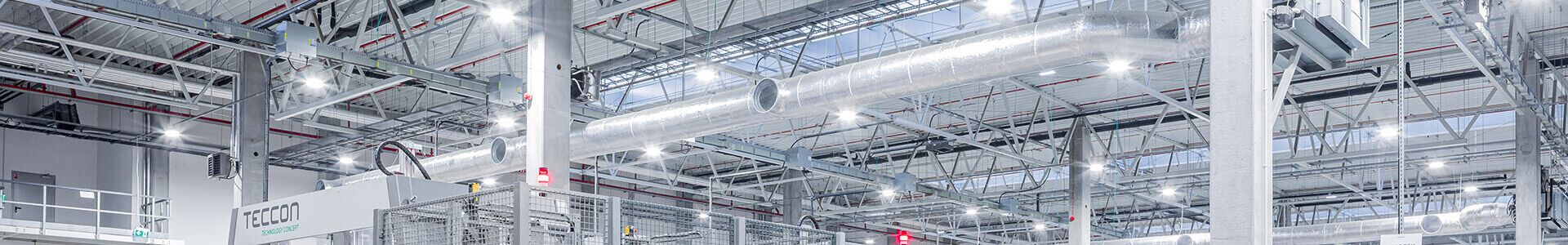 Un grand entrepôt équipé de rayonnages métalliques, éclairé par de nombreuses lampes, offrant de bonnes conditions de travail dans le secteur de l'électronique